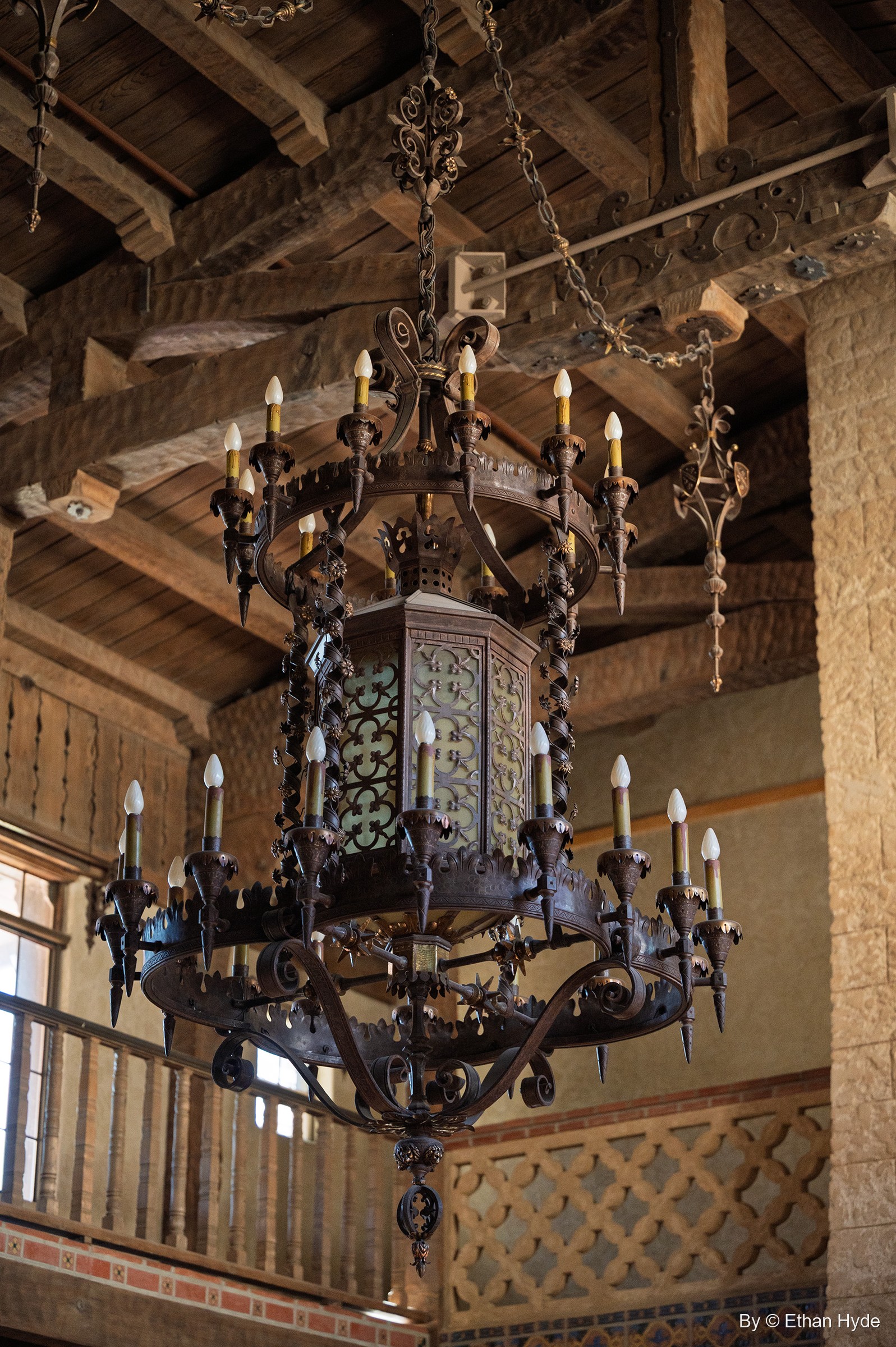 The wrought-iron chandelier of the Great Hall at Scotty's Castle, with the wooden balcony and beamed ceiling behind.
