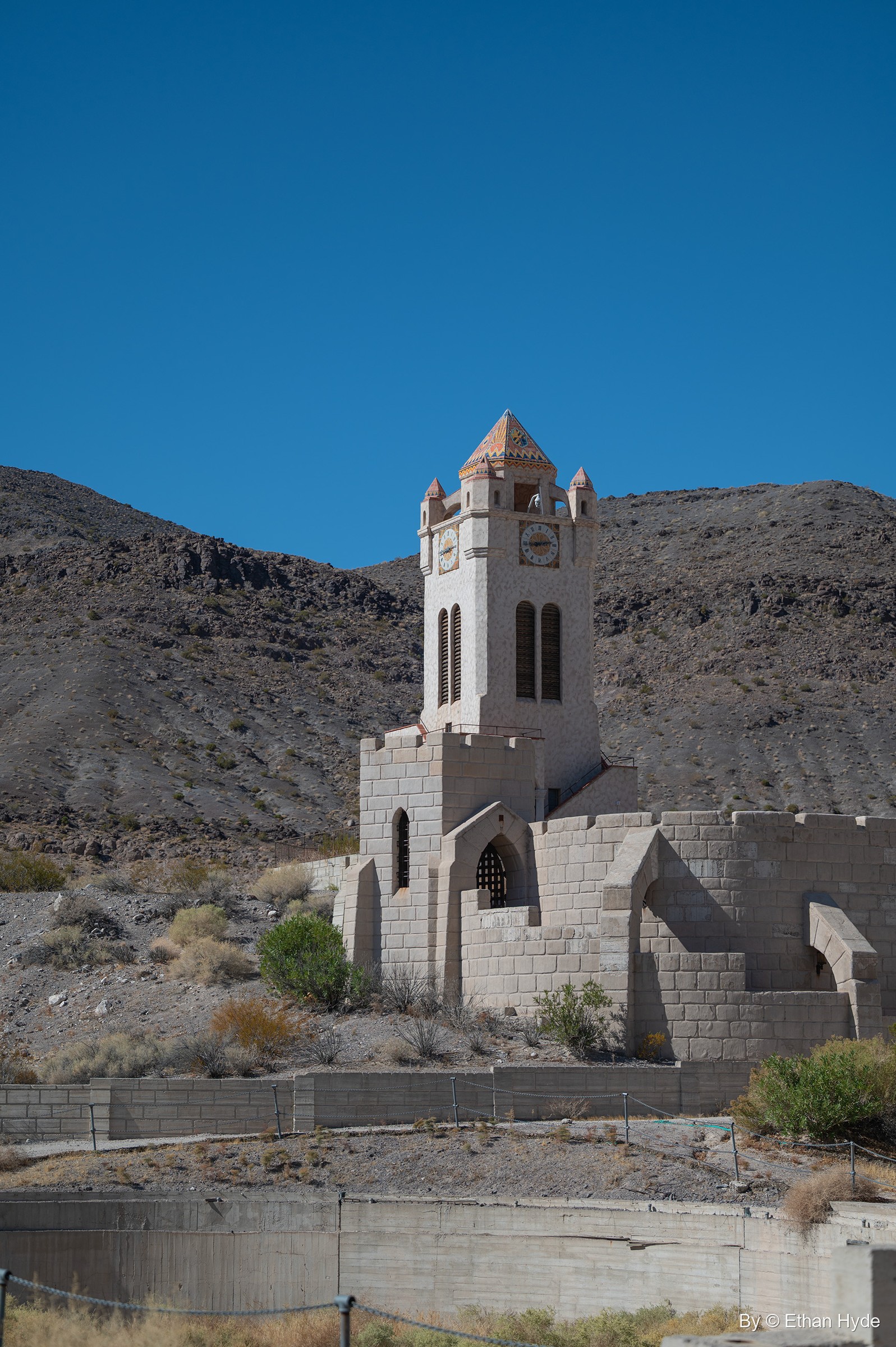 The freestanding Chimes Tower at Scotty's Castle rises behind crenellated walls beside the unfinished swimming pool, desert hills beyond.