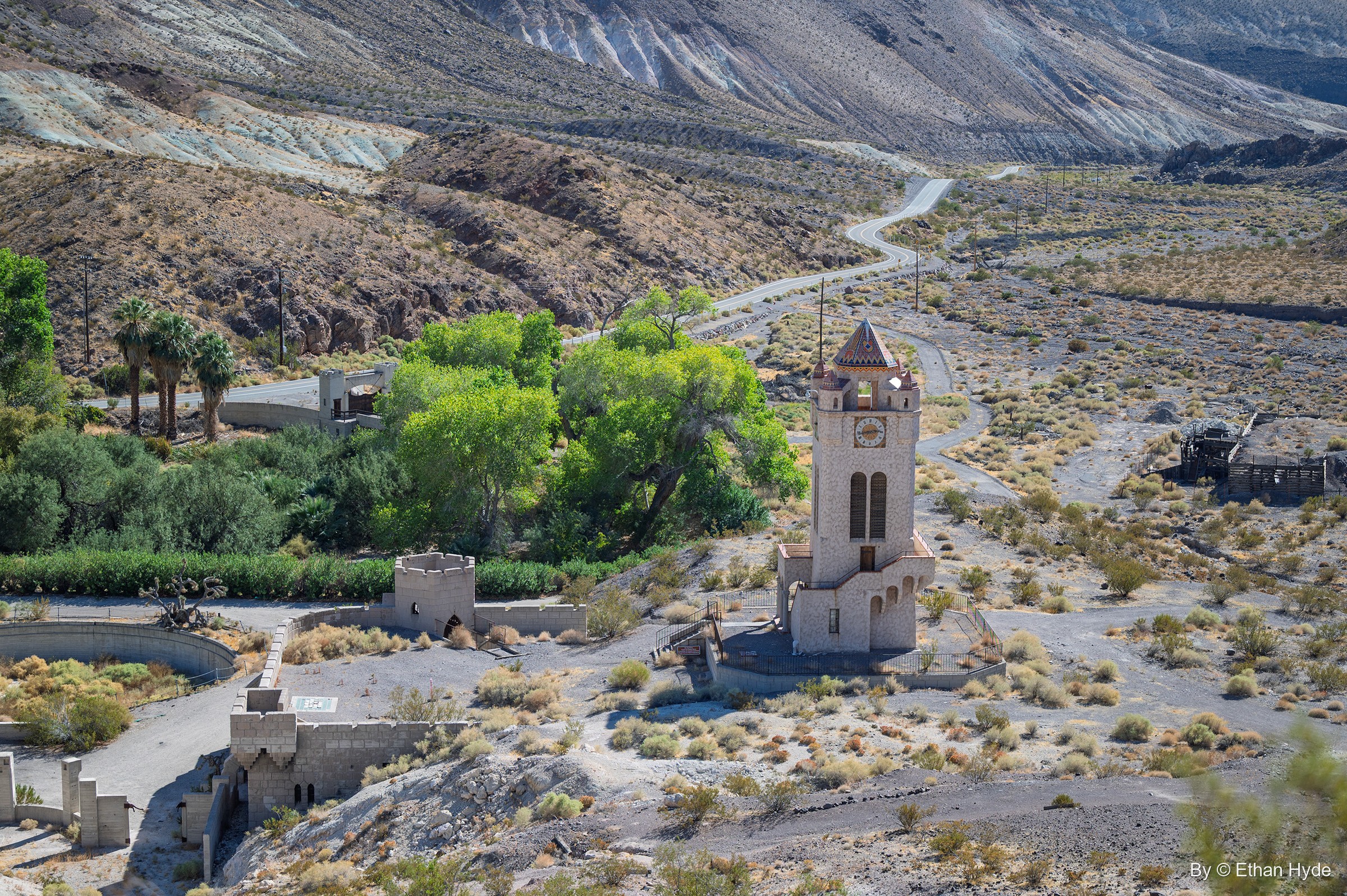 The Chimes Tower and the walls of the unfinished pool seen from above, the oasis trees beside them and the road winding up Grapevine Canyon.