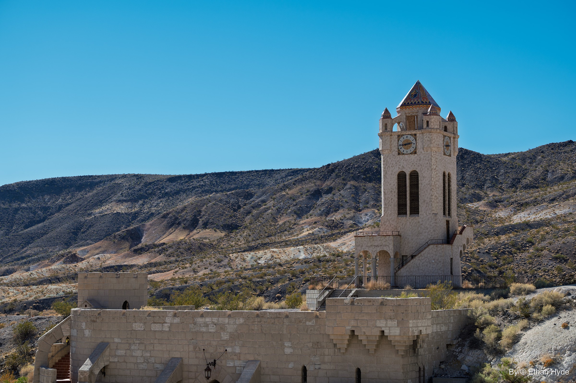 The Chimes Tower at Scotty's Castle stands on its hill above the crenellated walls of the unfinished pool, with desert mountains behind.
