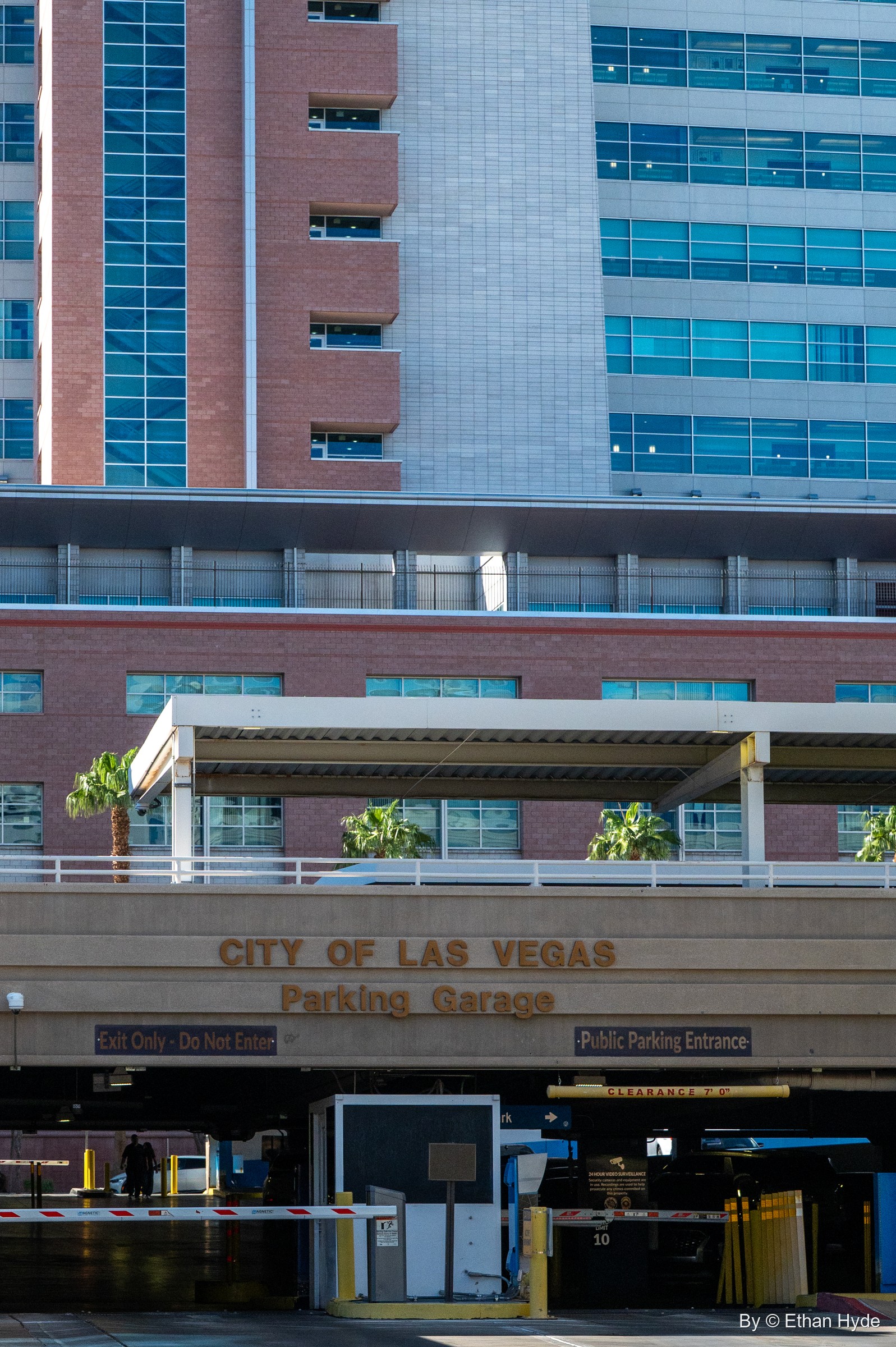 A city parking garage entrance beneath a canopy, with brick and blue-glass government towers stacked above.