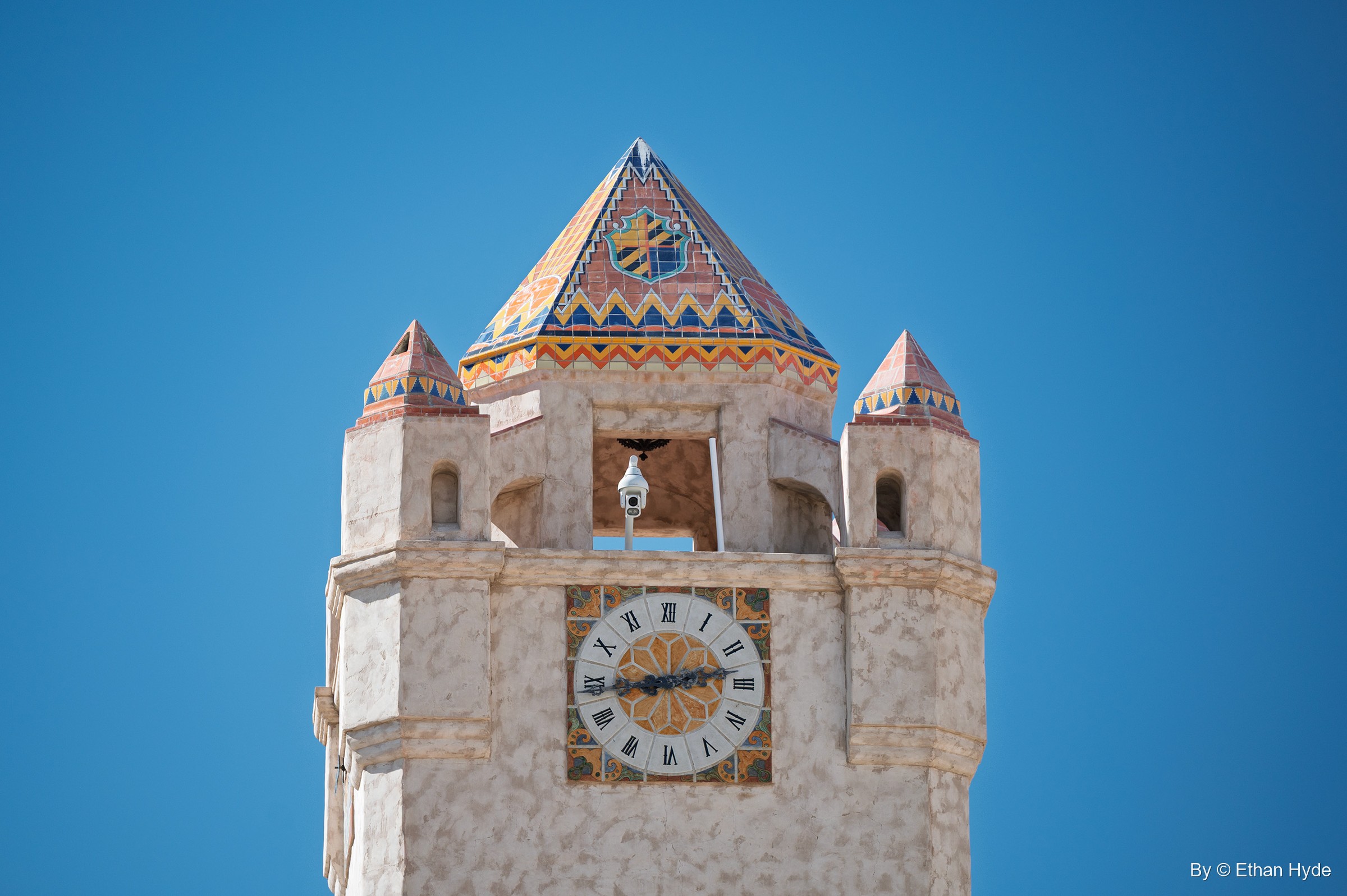 The top of the Chimes Tower at Scotty's Castle: clock face, open chime chamber and patterned tile roof against a blue sky.