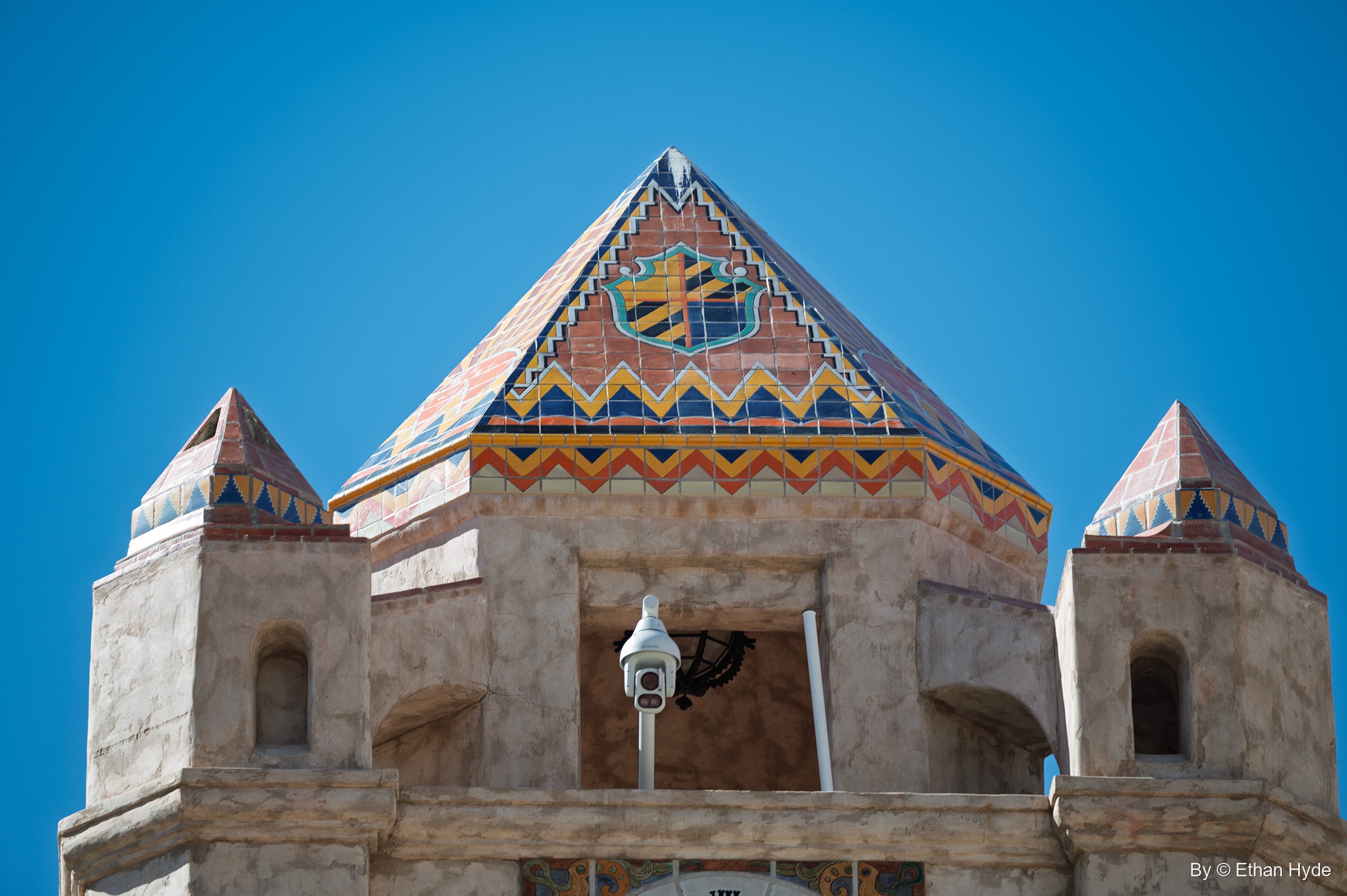 The patterned tile pyramid roof of the Chimes Tower at Scotty's Castle, with a coat of arms and zigzag bands between two small tiled turrets.