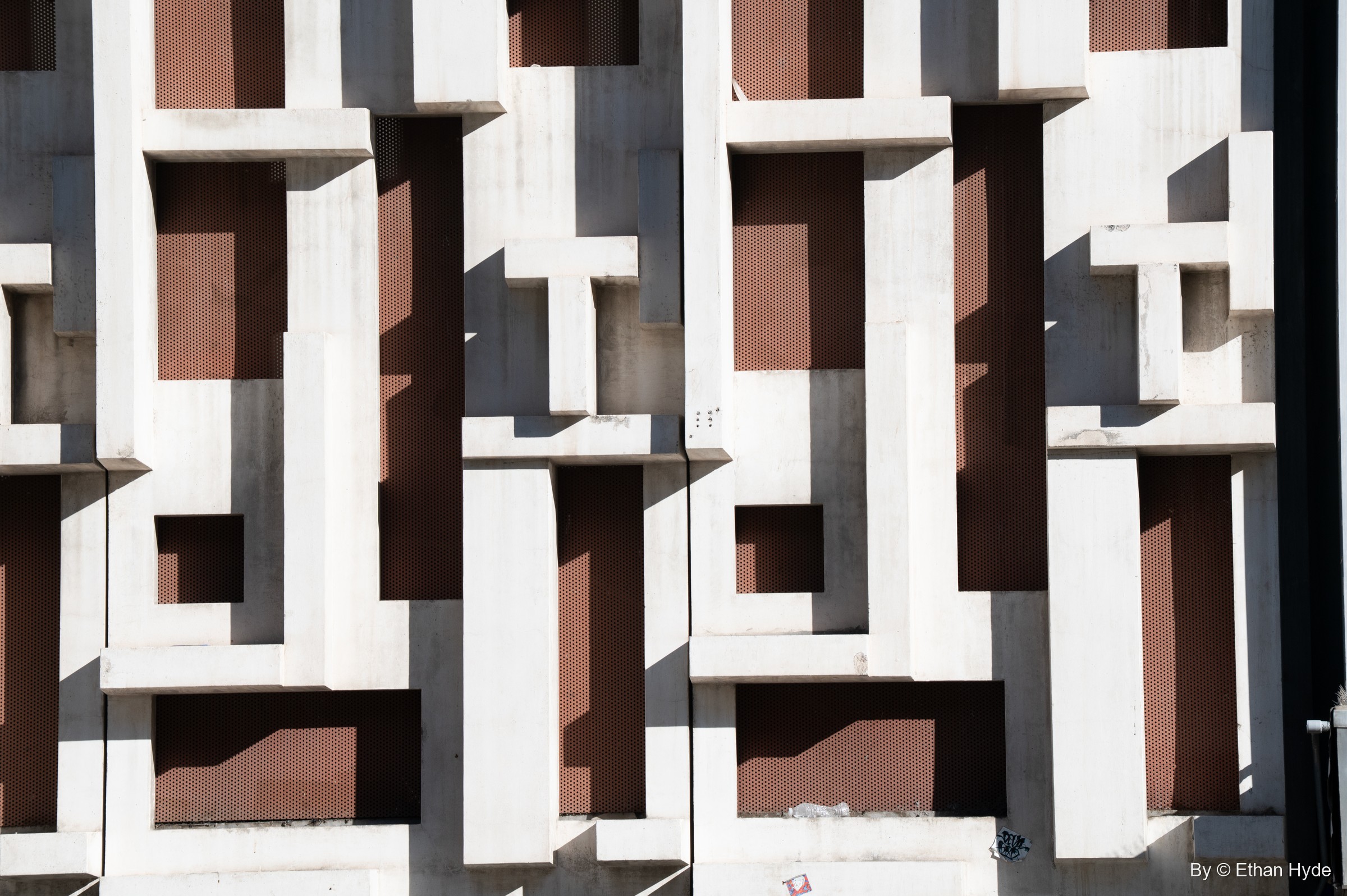 Abstract close-up of a white concrete facade of interlocking raised blocks over dark brown recesses.