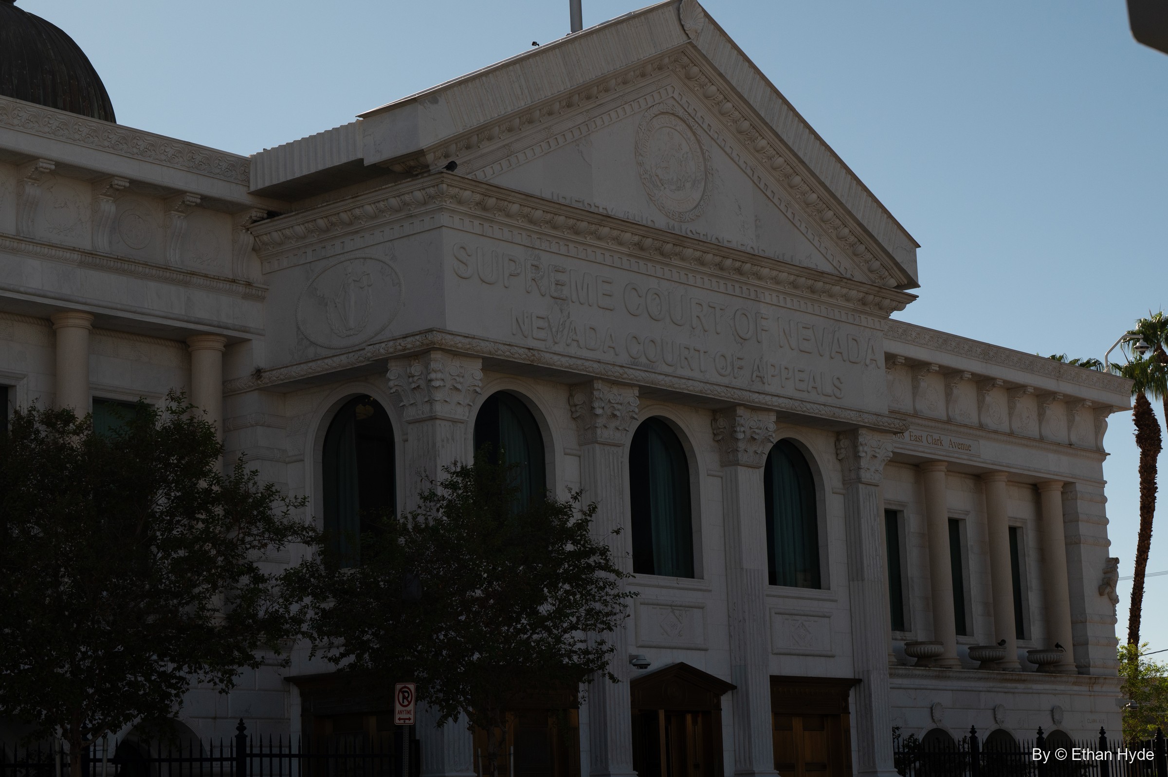 The white pediment and arched windows of the Nevada Supreme Court building in shadow, a palm at the edge.