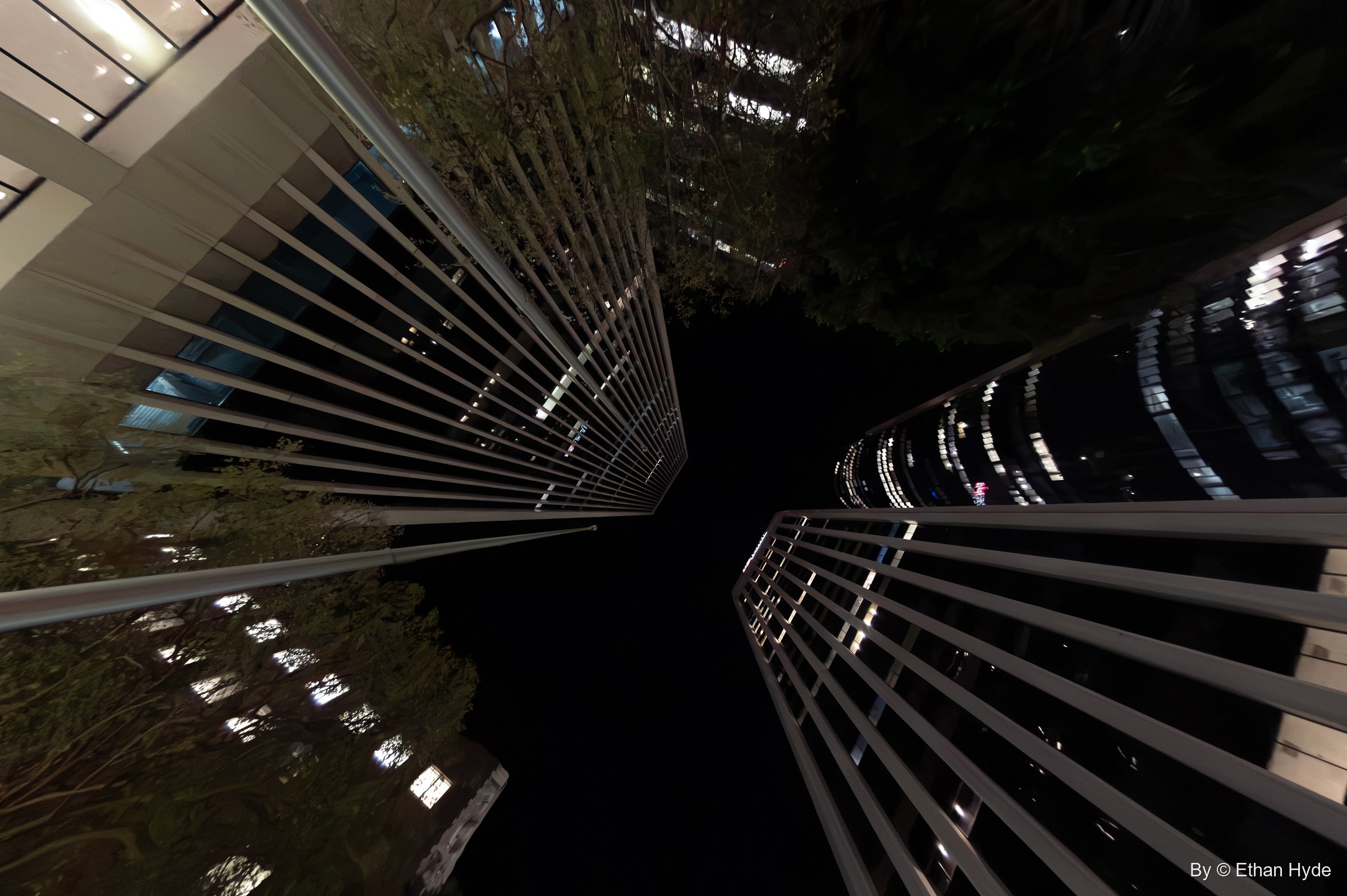 Looking straight up at night between two skyscrapers with horizontal fins, their lit floors converging on a black sky.