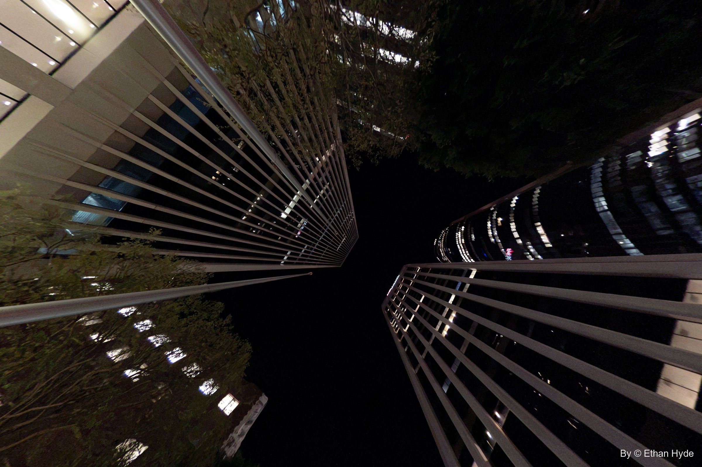 A wide upward view of finned glass towers at night, office lights glowing between the louvers.