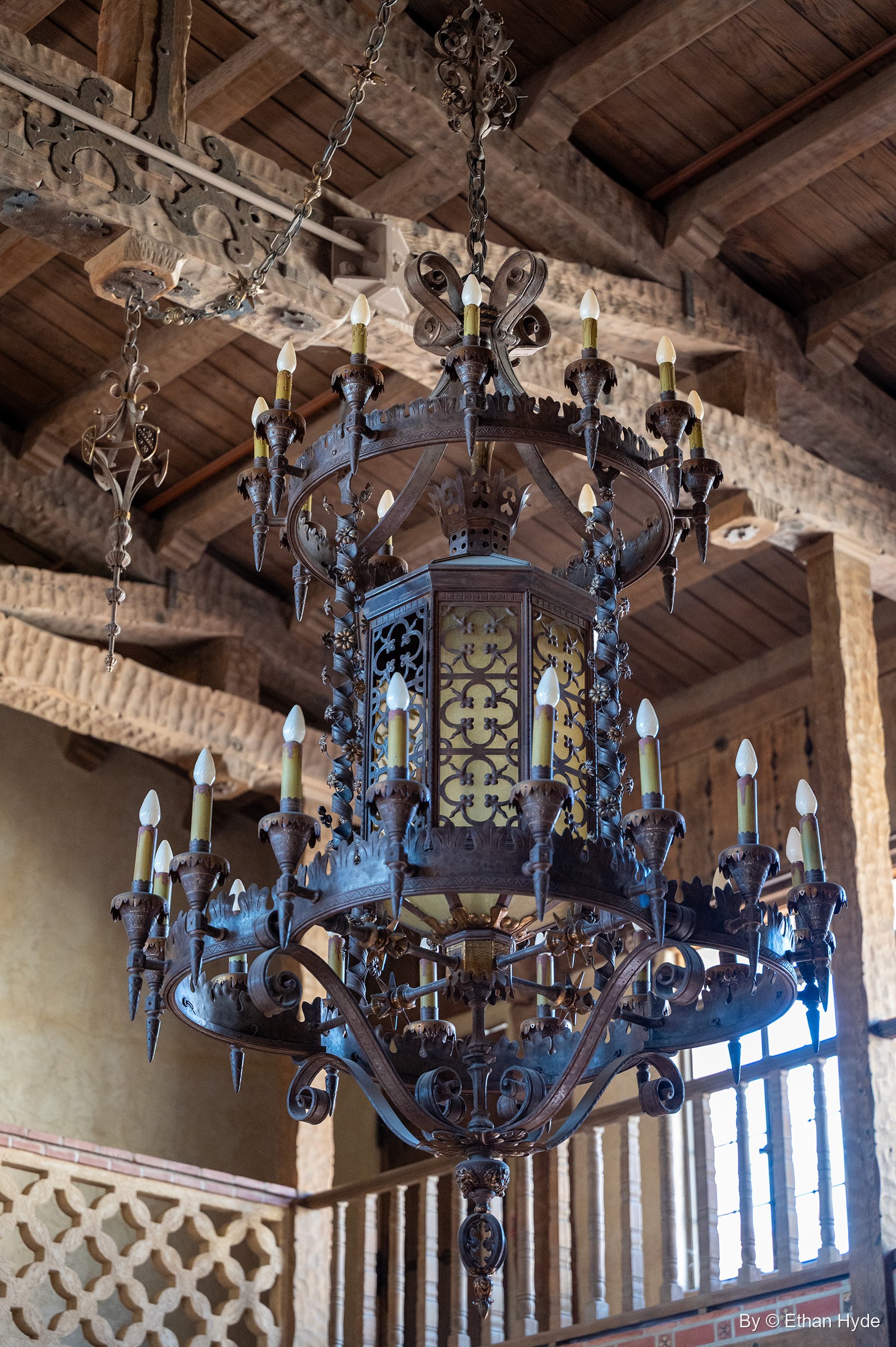 A hand-wrought iron chandelier hangs in the two-storey Great Hall at Scotty's Castle, beneath carved wooden beams.