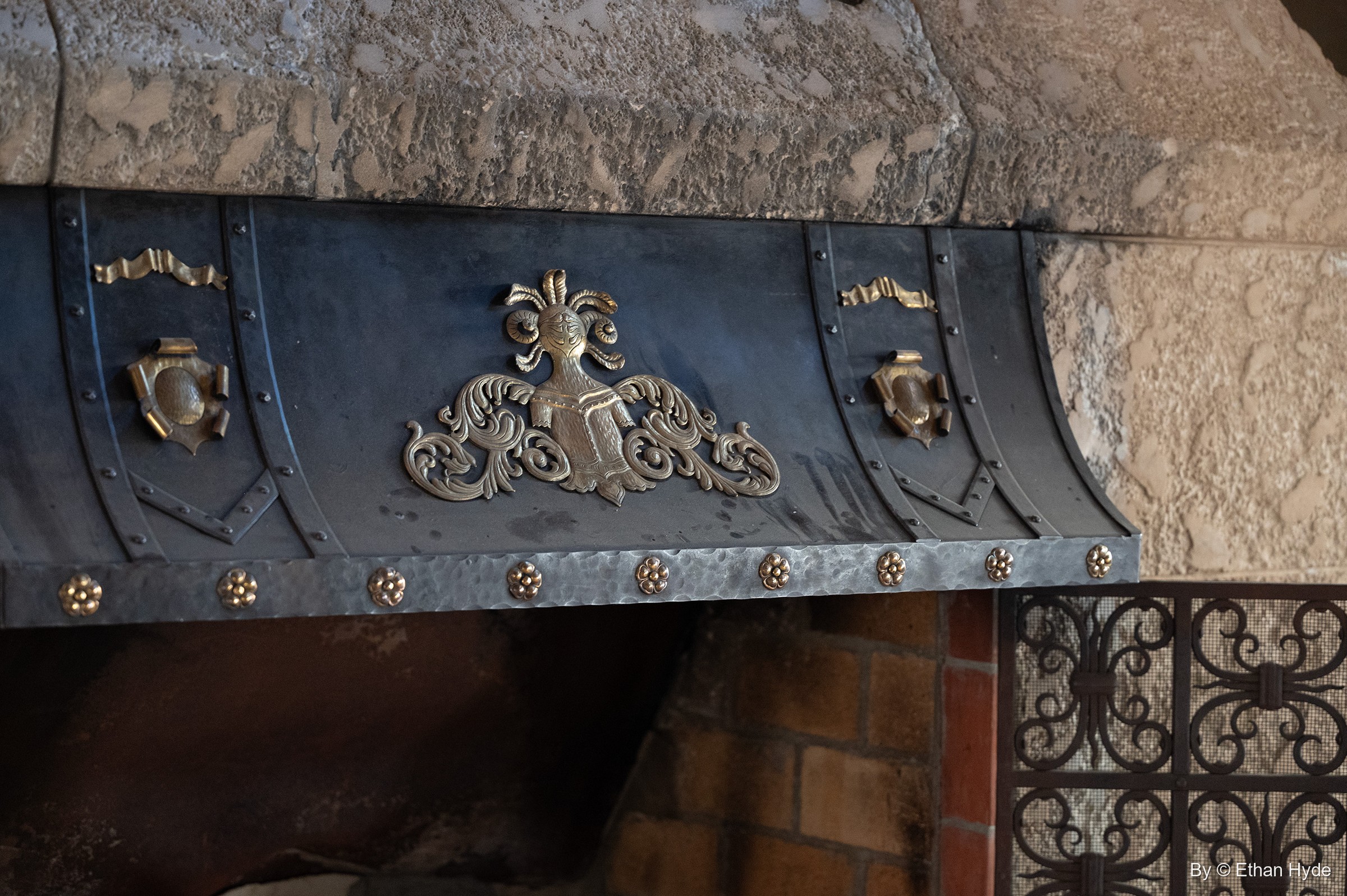 A dark iron hood with gilded crest and scroll ornaments above an iron grille inside Scotty's Castle.