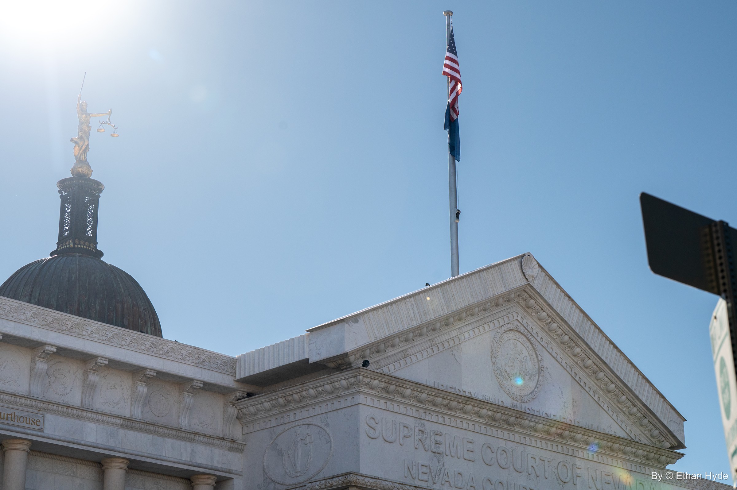 Looking up at the courthouse dome and Lady Justice statue with the sun flaring behind the flagpole.