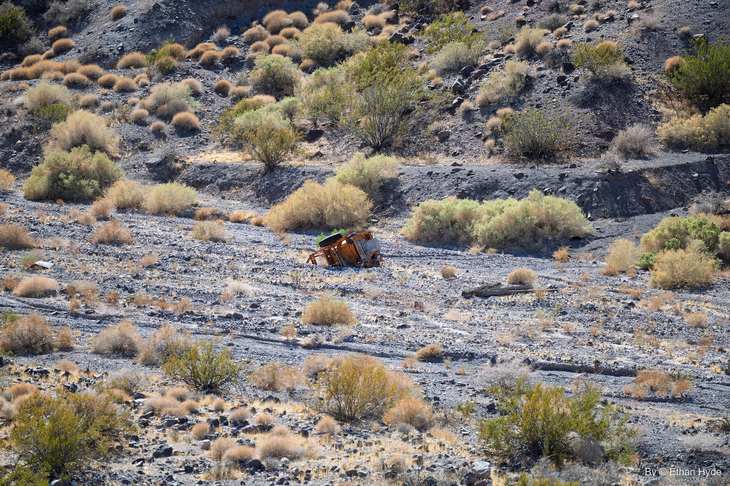 A small rusted vehicle body lying among desert scrub on a gravel slope near Scotty's Castle.