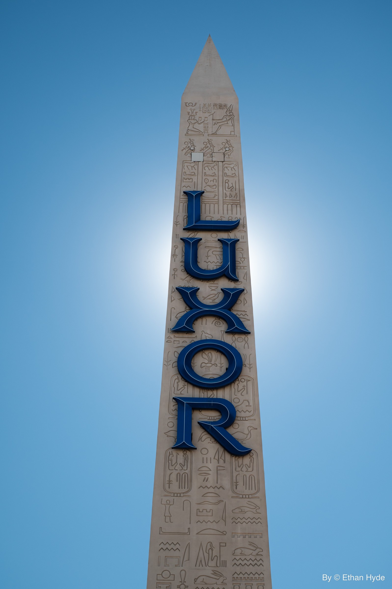 The vertical 'Luxor' sign rising against a bright blue sky.