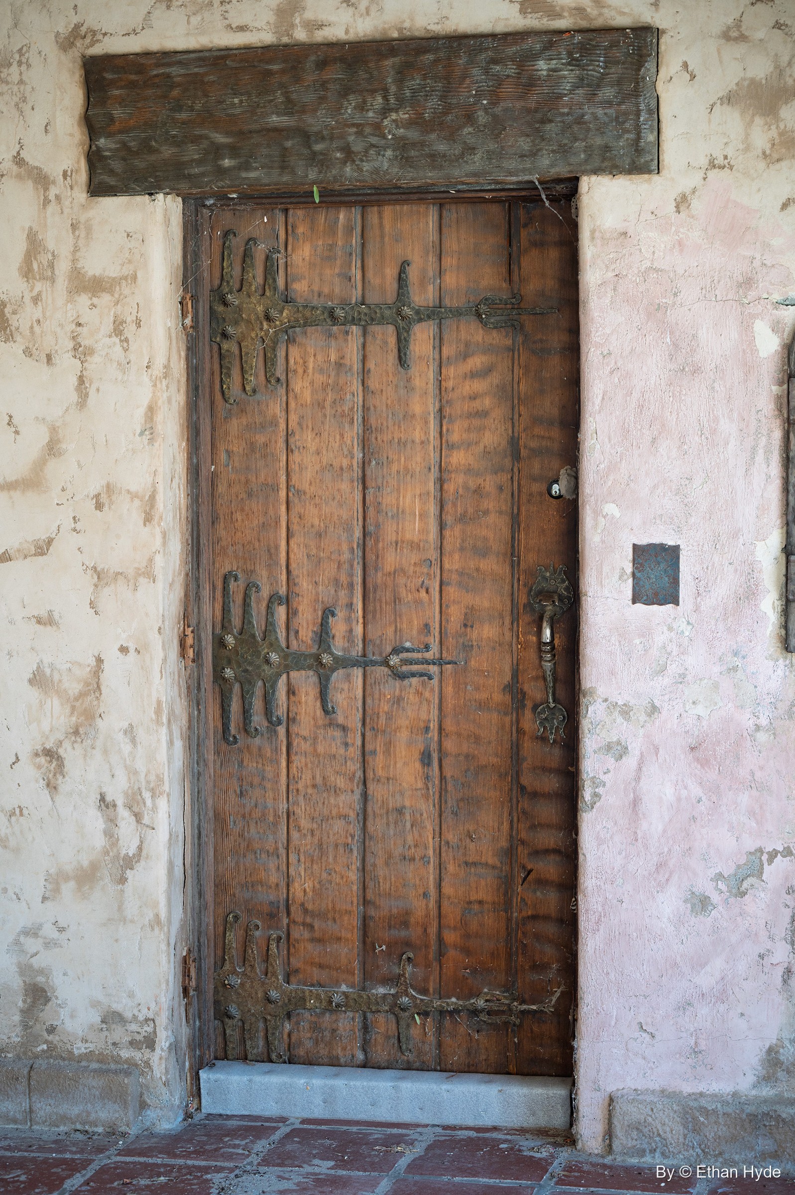 A weathered plank door with long iron strap hinges set in peeling pink stucco at Scotty's Castle.