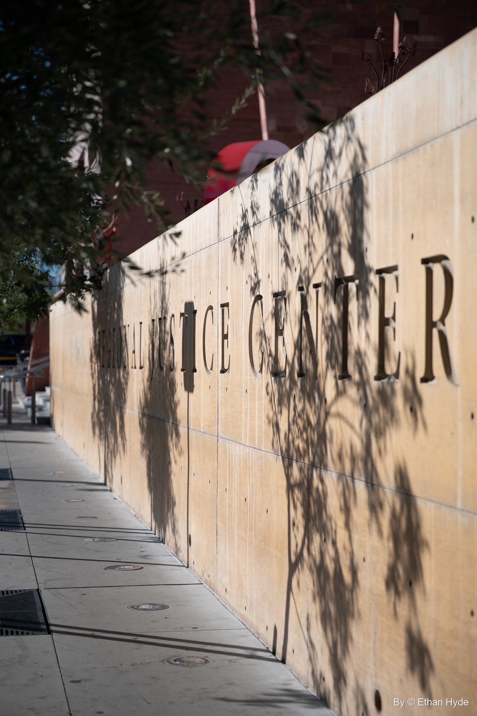 Large metal letters spell Regional Justice Center along a tan stone wall dappled with tree shadows.