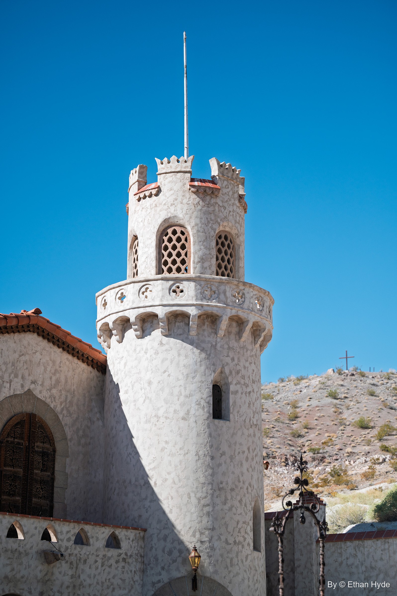 A round crenellated tower with lattice windows rises from the stucco walls of Scotty's Castle against a deep blue sky.
