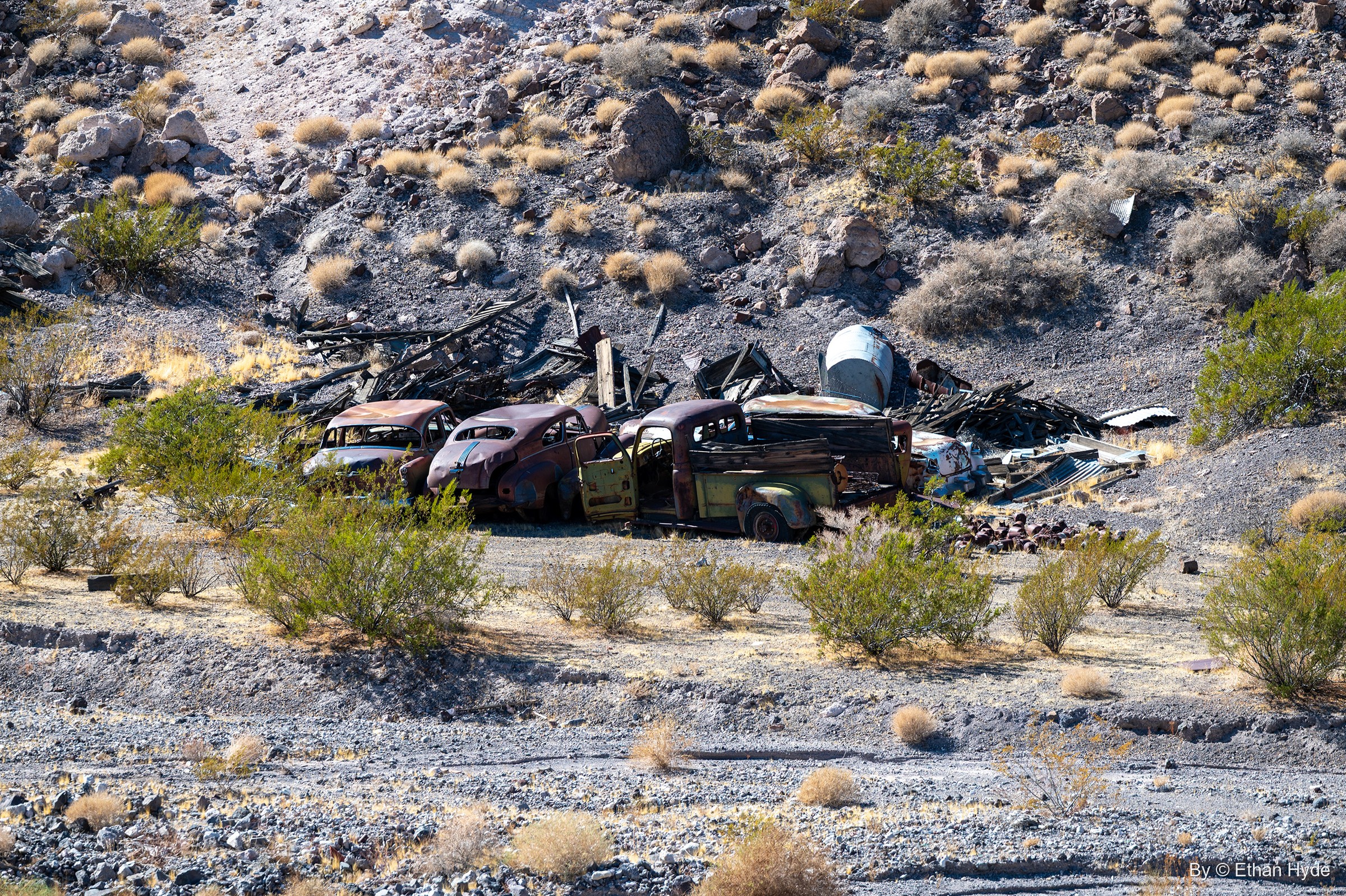 A row of rusted 1930s- and 1940s-style cars and trucks among scrap lumber on a desert slope near Scotty's Castle.