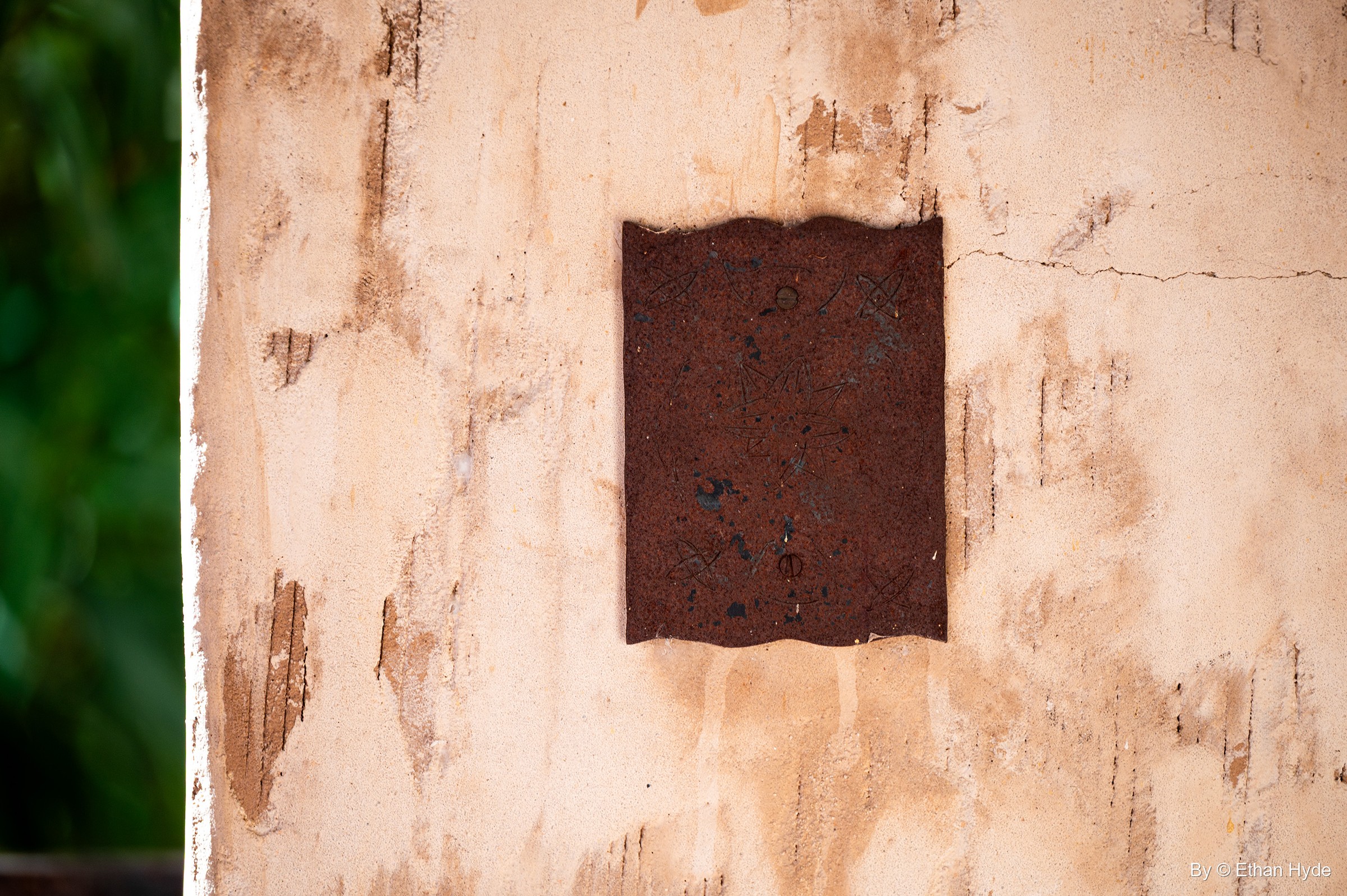 A rusted wavy-edged metal plate on a stained stucco wall at Scotty's Castle.