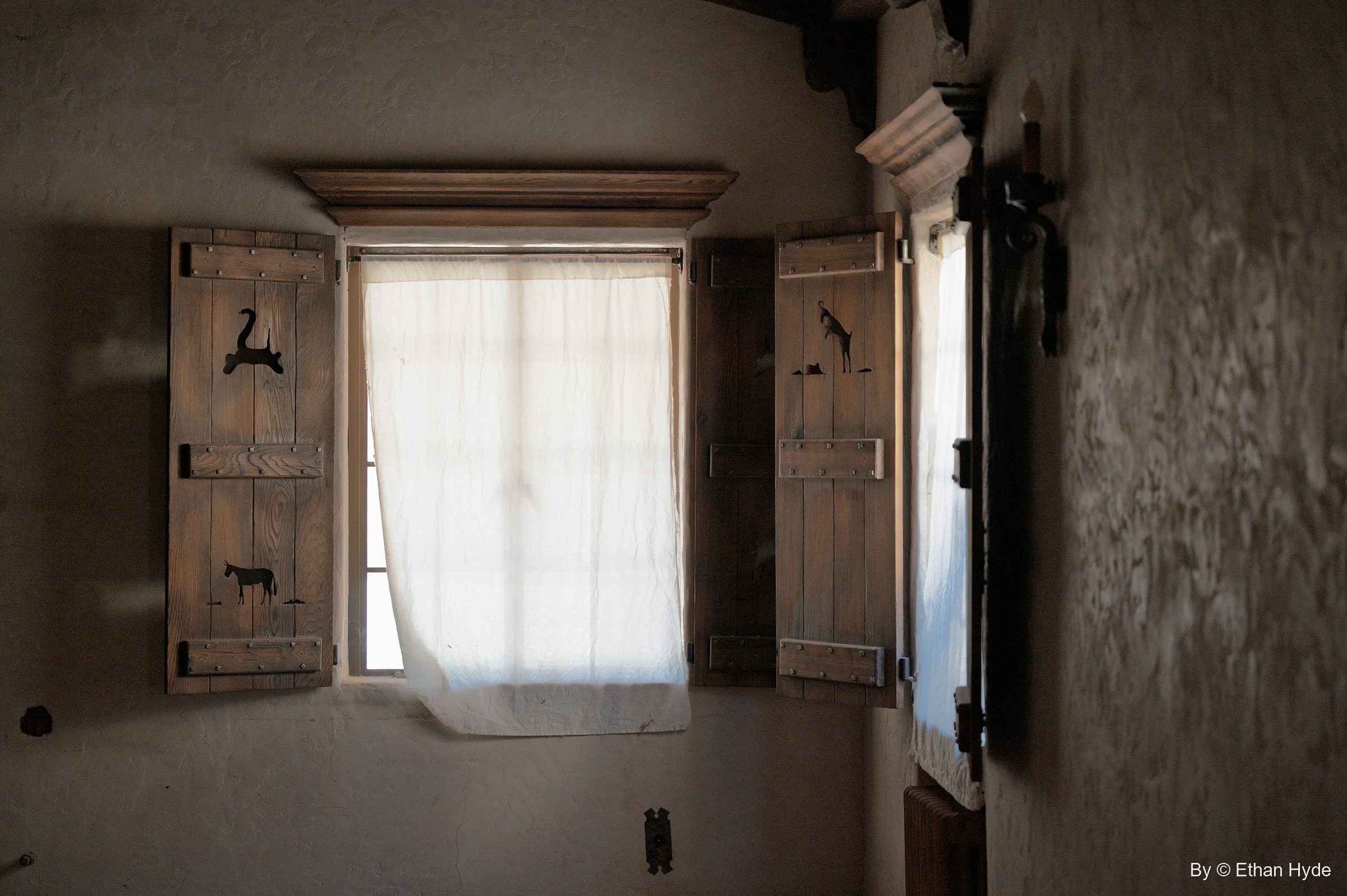 Light through a curtained window inside Scotty's Castle, flanked by wooden shutters cut out with desert animal silhouettes.