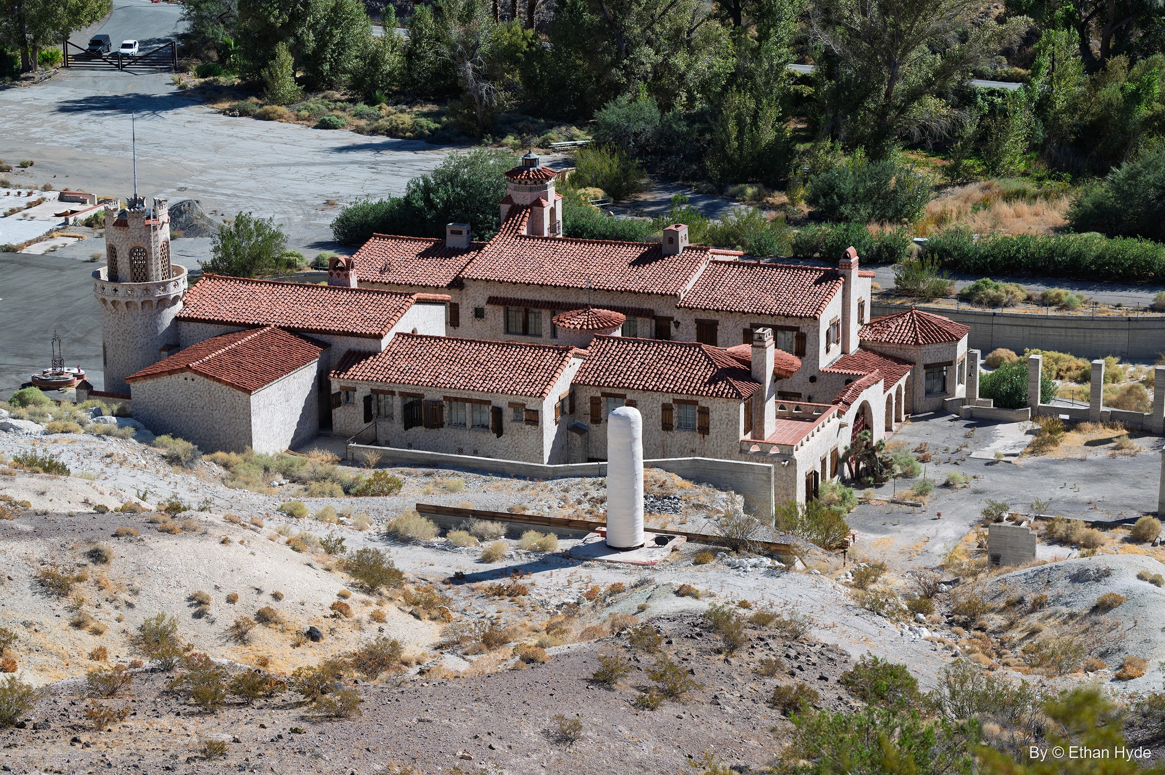 An elevated view of the main house and annex of Scotty's Castle, red roofs and towers set on pale desert ground beside the oasis.