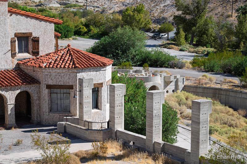 An elevated view over a round tile-roofed building and stucco walls at Scotty's Castle toward the green oasis of Grapevine Canyon.
