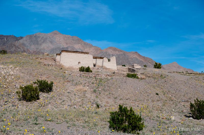 Crumbling concrete walls of the Ashford Mill office on a scrubby hillside below rugged mountains.