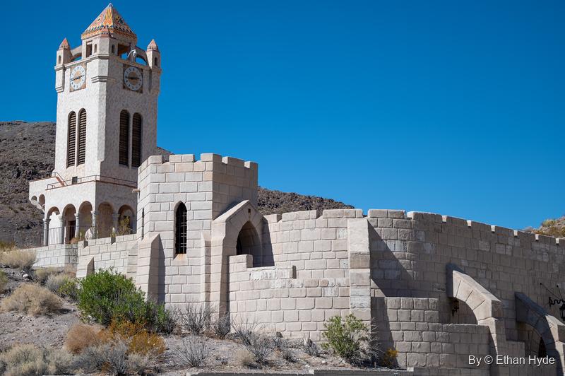 The Chimes Tower at Scotty's Castle above crenellated stone-block walls on a dry desert slope.