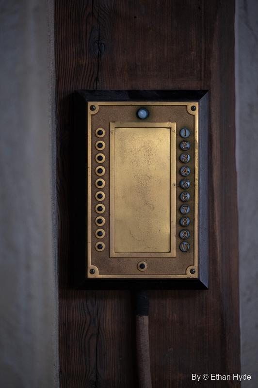 A brass servant call-button (annunciator) panel on a dark wooden post, Scotty's Castle.