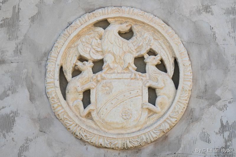 A carved circular medallion of a coat of arms with an eagle crest and two heraldic animals, set into a stucco wall at Scotty's Castle.