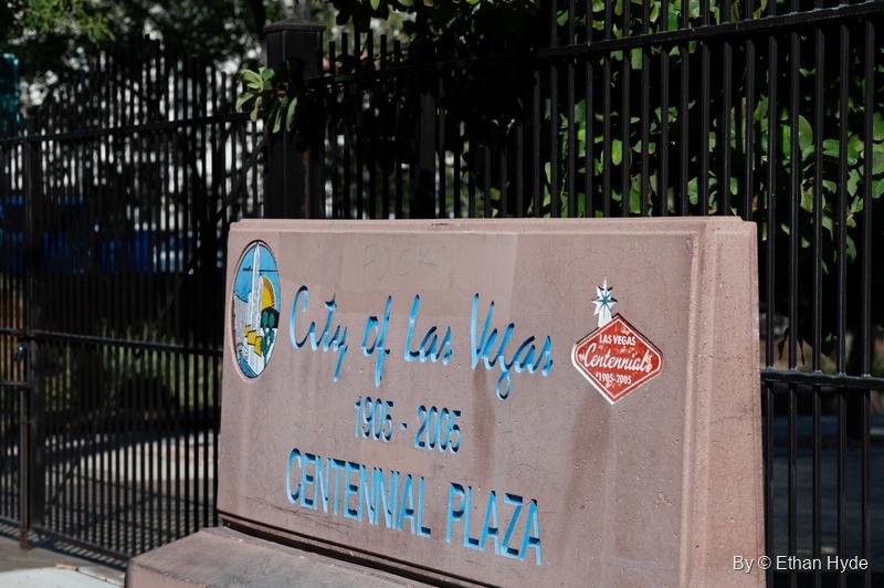 A pink stone marker for the city's Centennial Plaza, 1905 to 2005, in front of a tall black iron fence.