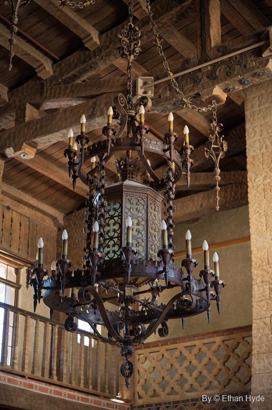 The wrought-iron chandelier of the Great Hall at Scotty's Castle, with the wooden balcony and beamed ceiling behind.
