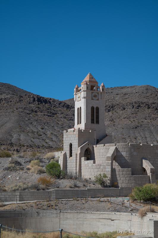 The freestanding Chimes Tower at Scotty's Castle rises behind crenellated walls beside the unfinished swimming pool, desert hills beyond.