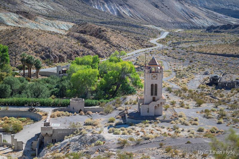 The Chimes Tower and the walls of the unfinished pool seen from above, the oasis trees beside them and the road winding up Grapevine Canyon.