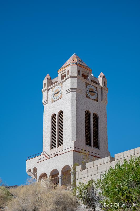 Looking up at the Chimes Tower at Scotty's Castle: clock faces, louvered belfry openings and an arcaded base against a deep blue sky.