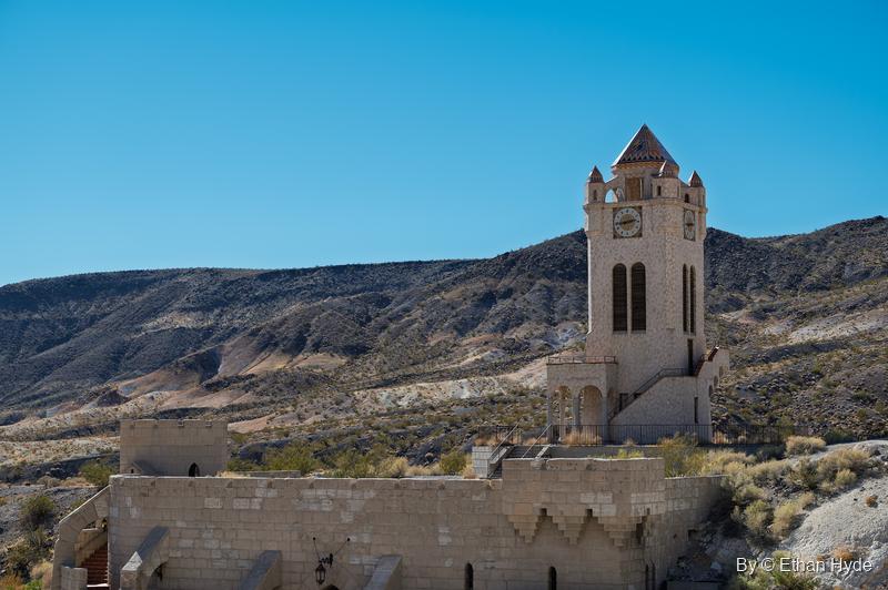 The Chimes Tower at Scotty's Castle stands on its hill above the crenellated walls of the unfinished pool, with desert mountains behind.