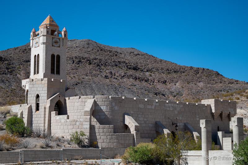 The Chimes Tower at Scotty's Castle with its clock and tiled roof, standing above crenellated walls near the unfinished pool.