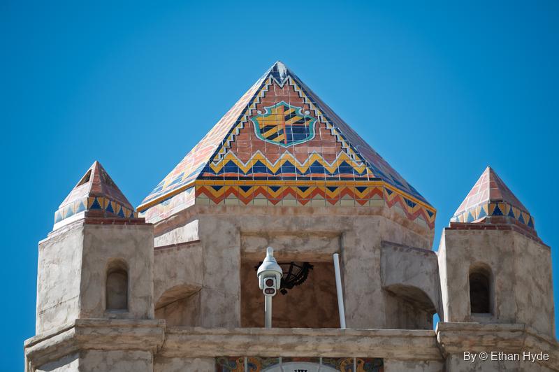 The patterned tile pyramid roof of the Chimes Tower at Scotty's Castle, with a coat of arms and zigzag bands between two small tiled turrets.