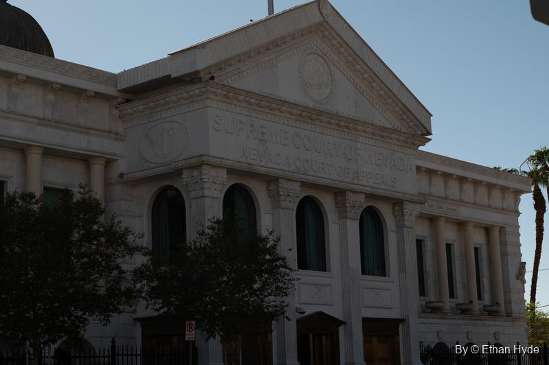 The white pediment and arched windows of the Nevada Supreme Court building in shadow, a palm at the edge.