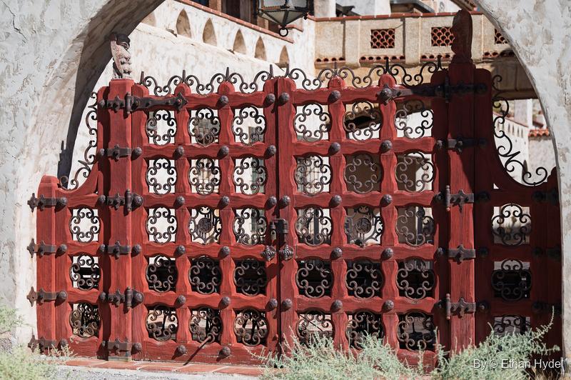 Red wood-and-wrought-iron courtyard gates at Scotty's Castle, a grid of scrolled iron panels under a stucco arch.