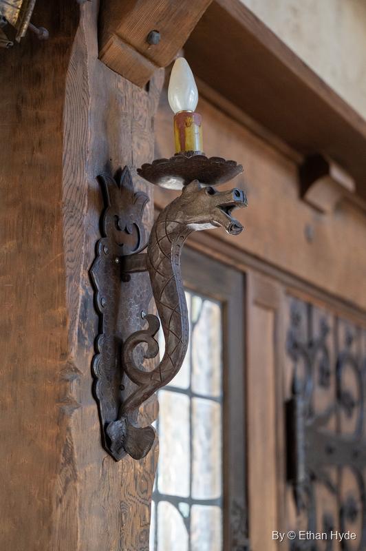 A wrought-iron dragon-form wall sconce on a carved wooden post inside Scotty's Castle, one of the iron fixtures made for each room.