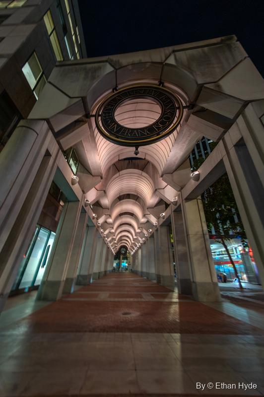 Looking down a vaulted, lit arcade at night beneath a bronze ring reading "Federal Reserve Bank of San Francisco."