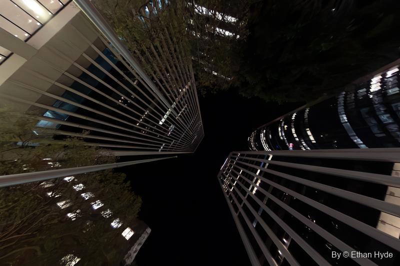 Looking straight up at night between two skyscrapers with horizontal fins, their lit floors converging on a black sky.