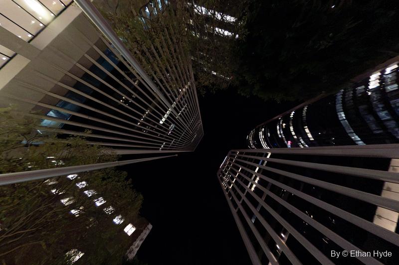 A wide upward view of finned glass towers at night, office lights glowing between the louvers.