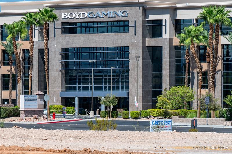 The granite and glass entrance of a corporate office building, framed by tall palm trees and trimmed shrubs, beyond a graded dirt lot.