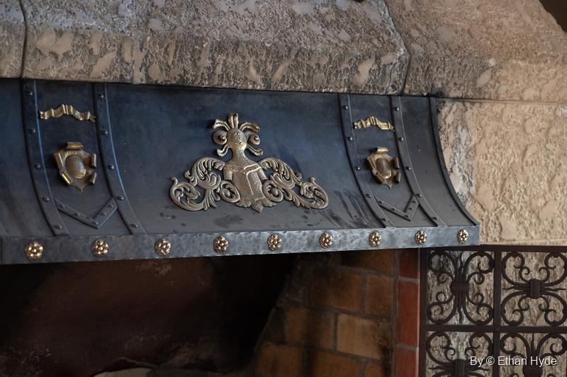 A dark iron hood with gilded crest and scroll ornaments above an iron grille inside Scotty's Castle.