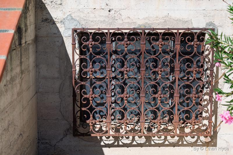A scrolled wrought-iron window grille casting its shadow on a stucco wall at Scotty's Castle, pink oleander at the edge.