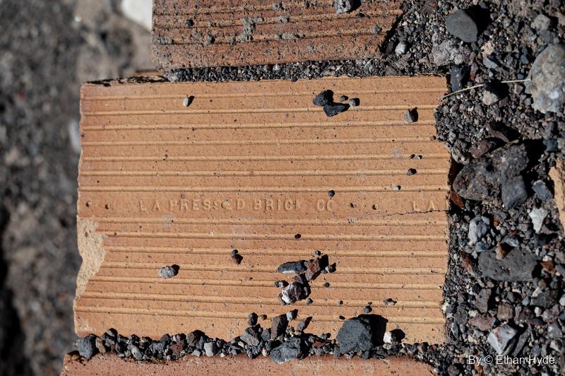 A ribbed clay block stamped "L.A. Pressed Brick Co." half buried in volcanic gravel near Scotty's Castle.