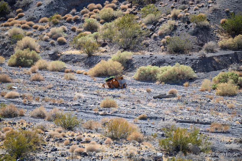 A small rusted vehicle body lying among desert scrub on a gravel slope near Scotty's Castle.