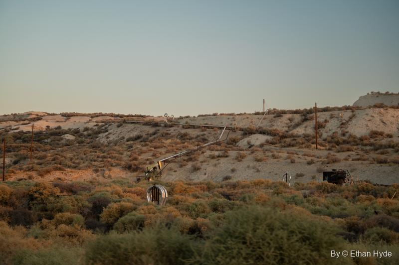 Early light on a scrubby hillside of the McKittrick oil field, scattered with pipes, wellheads and power poles.