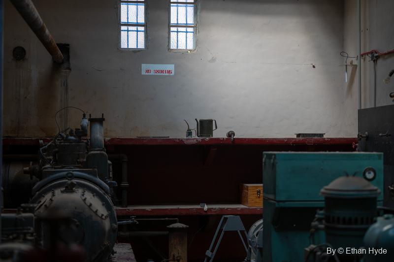 Inside the Powerhouse at Scotty's Castle, dark generating machinery lit by light from high windows on a pale wall.