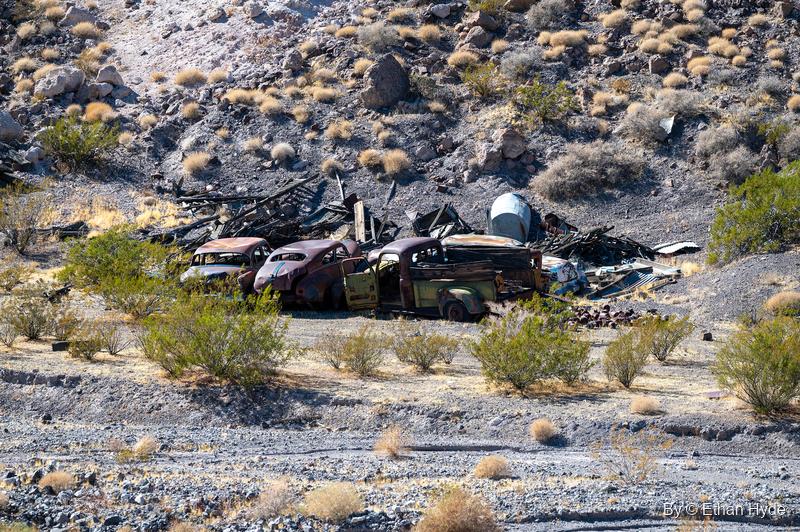 A row of rusted 1930s- and 1940s-style cars and trucks among scrap lumber on a desert slope near Scotty's Castle.